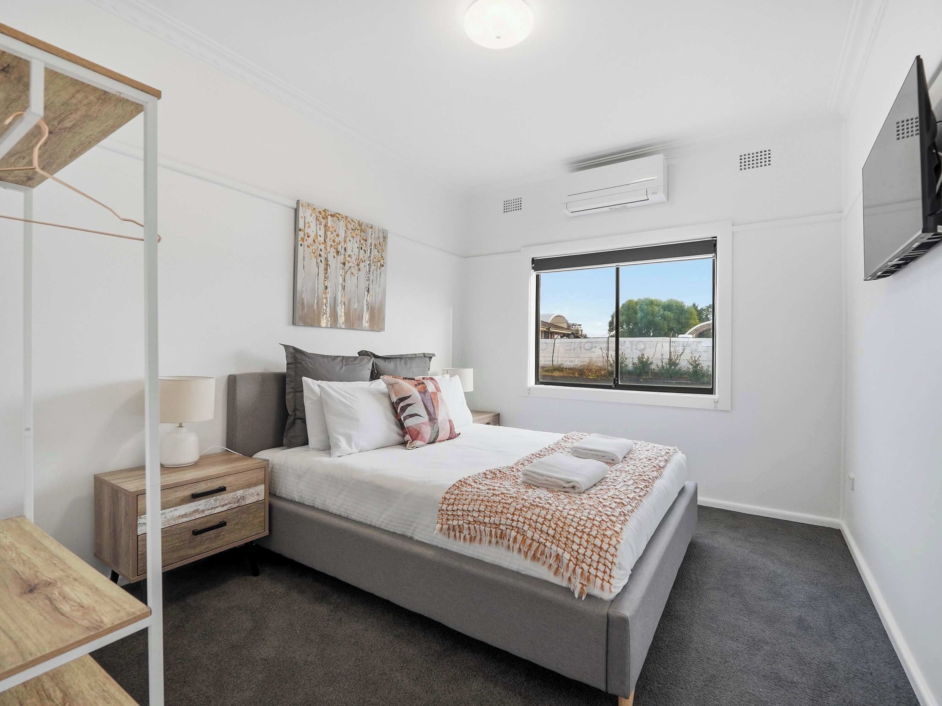 A bedroom with a bed, bedside table, lamp, and a window with a view.