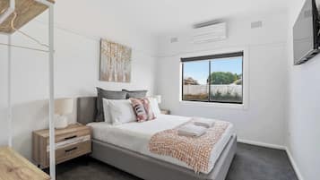 A bedroom with a bed, bedside table, lamp, and a window with a view.