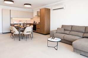 A modern living room with a sofa, a dining area with chairs and a table, and a kitchen with cabinets and appliances. - Pool And Sea - Modern Apart Sannat Gozo (Sannat)