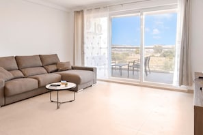 A modern living room with a sofa, a small round table, and a view of a landscape through large windows. - Pool And Sea - Modern Apart Sannat Gozo (Sannat)