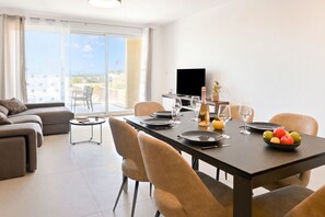 A modern living room with a dining area, a flat-screen TV, and a balcony with a view. - Pool And Sea - Modern Apart Sannat Gozo (Sannat)