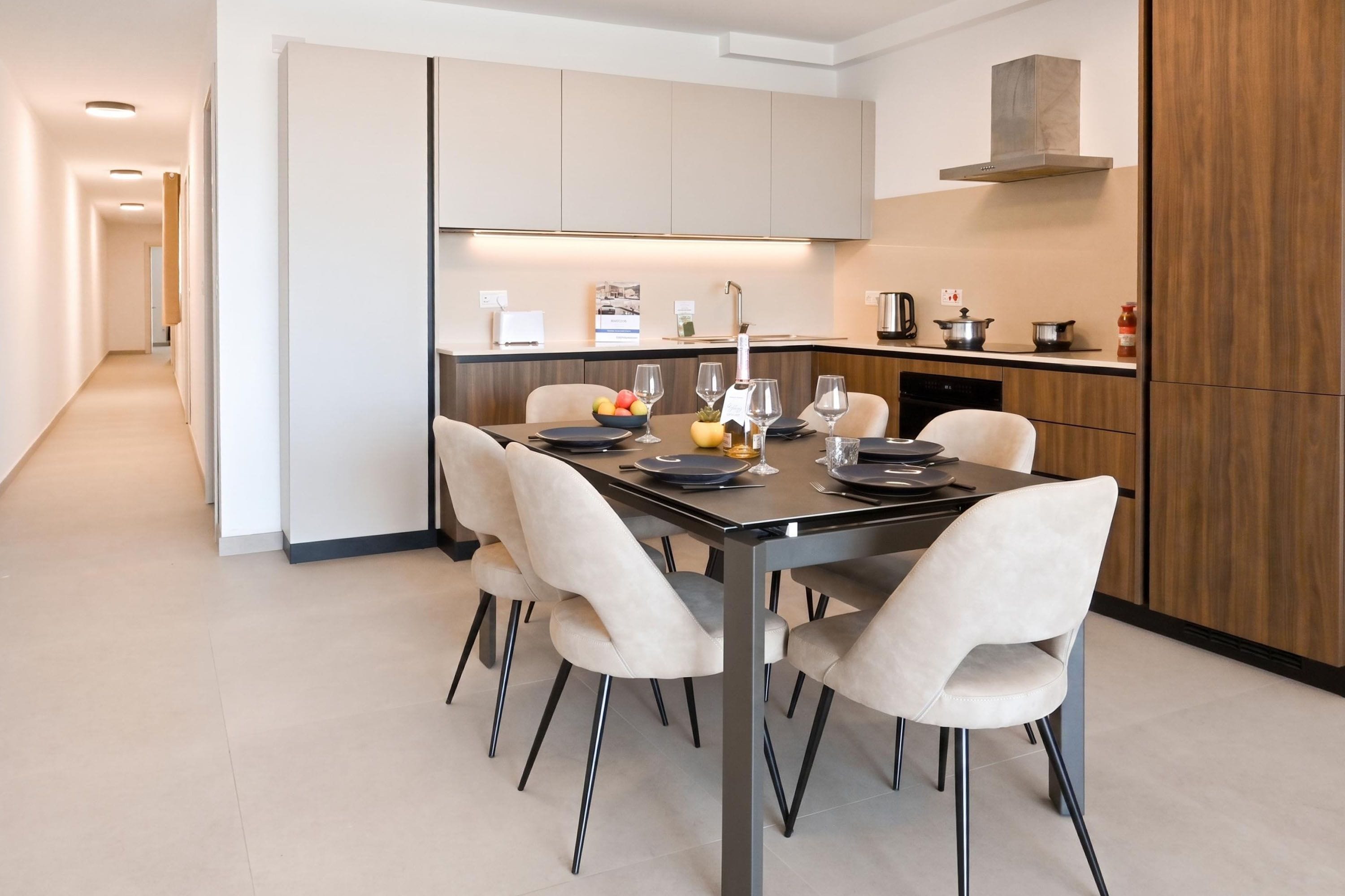 A modern kitchen with a dining area, featuring a central island, built-in cabinets, and a stainless steel range hood.
