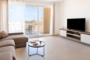 Ein modernes Wohnzimmer mit einer Couch, einem Couchtisch, einem Flachbildfernseher und einer Schiebetür zu einem Außenbalkon.