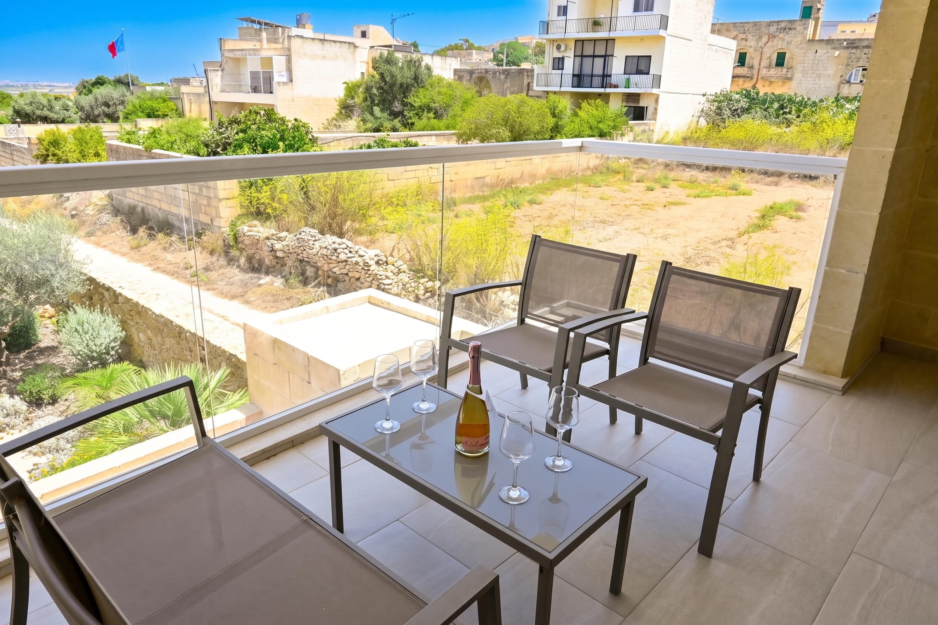 A balcony with a table and chairs, a bottle of wine, and a view of the surrounding buildings and landscape.