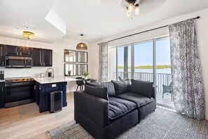 A modern kitchen with dark cabinetry, a dining area with a gray sofa, and large windows offering a view of the outdoors. - Forever Sunshine - Fully Renovated (St. Petersburg)