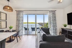 A modern living room with a sofa, dining table, chairs, and a balcony with a view of a bridge. - Forever Sunshine - Fully Renovated (St. Petersburg)