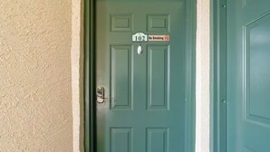 Eine türkisblaue Tür mit einem Rauchverbot-Schild und der Hausnummer 102 an einer beigen Wand.