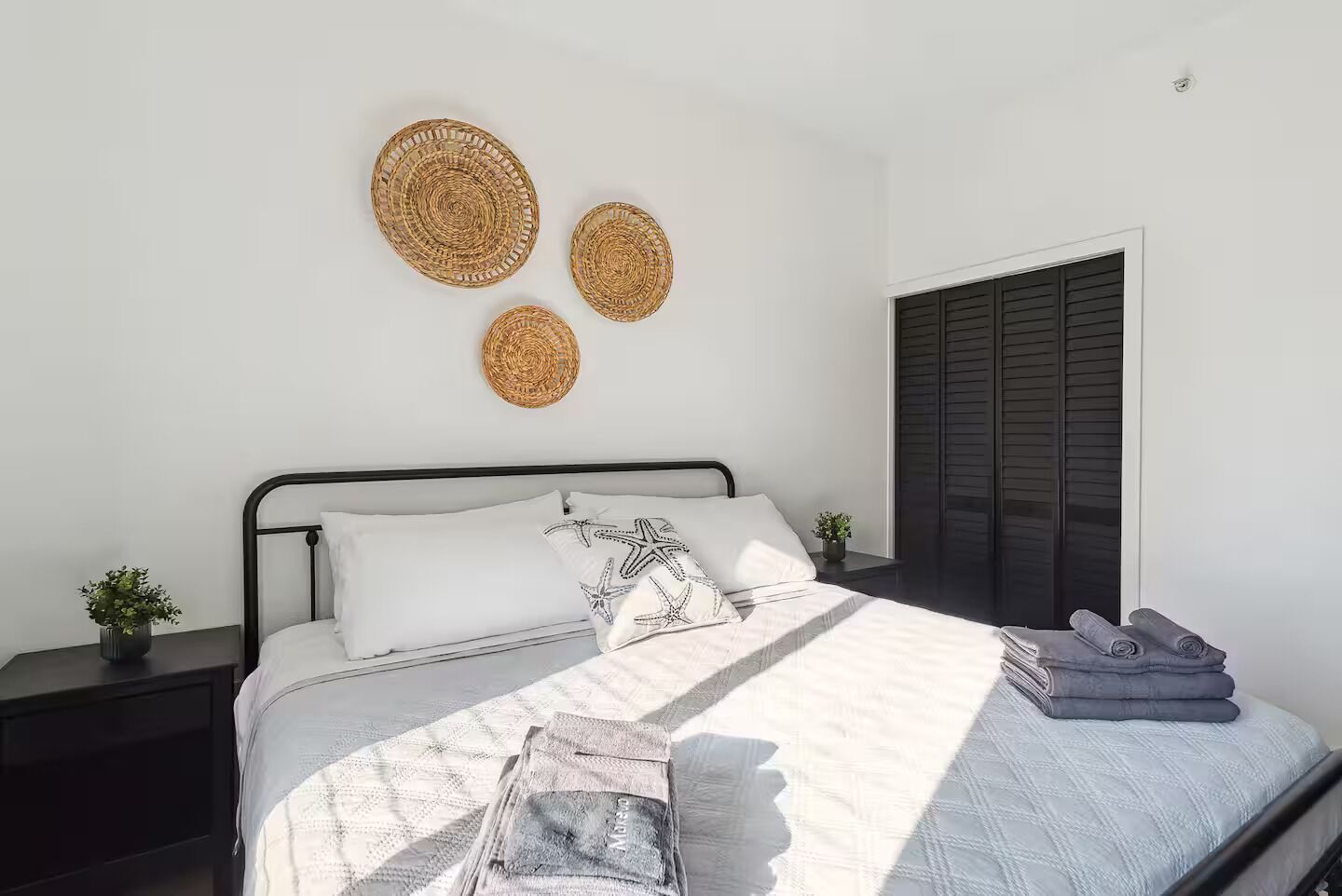 A bedroom with a bed, pillows, a bedside table with a plant, and a window with blinds.