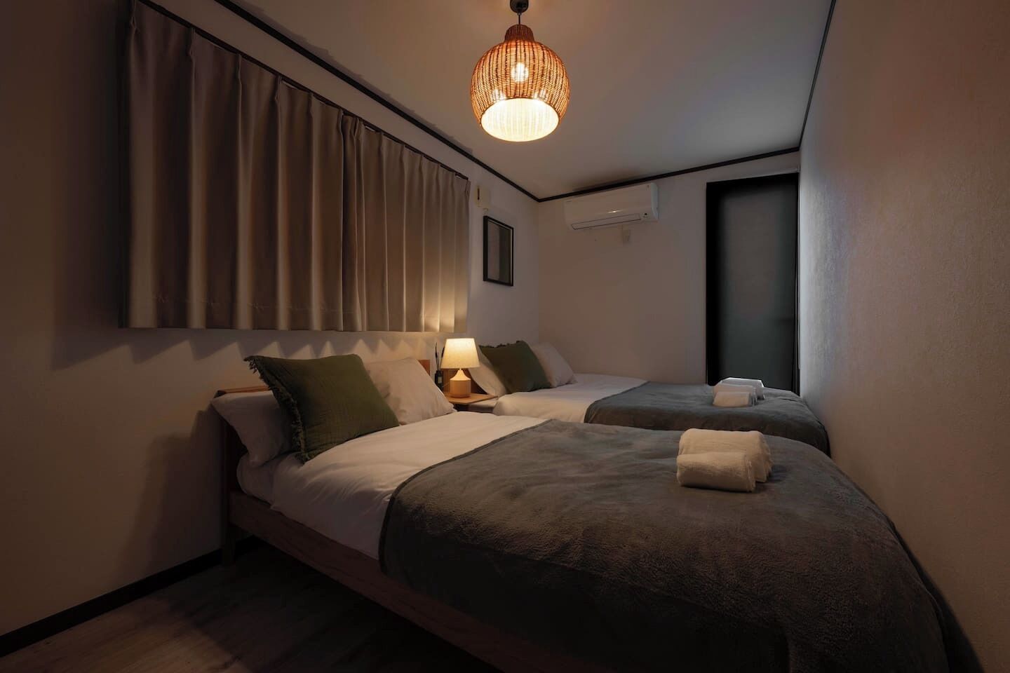 A hotel room with two beds, a bedside lamp, a window, and a hanging light fixture.