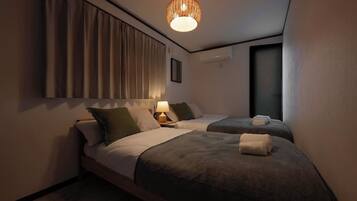A hotel room with two beds, a bedside lamp, a window, and a hanging light fixture.