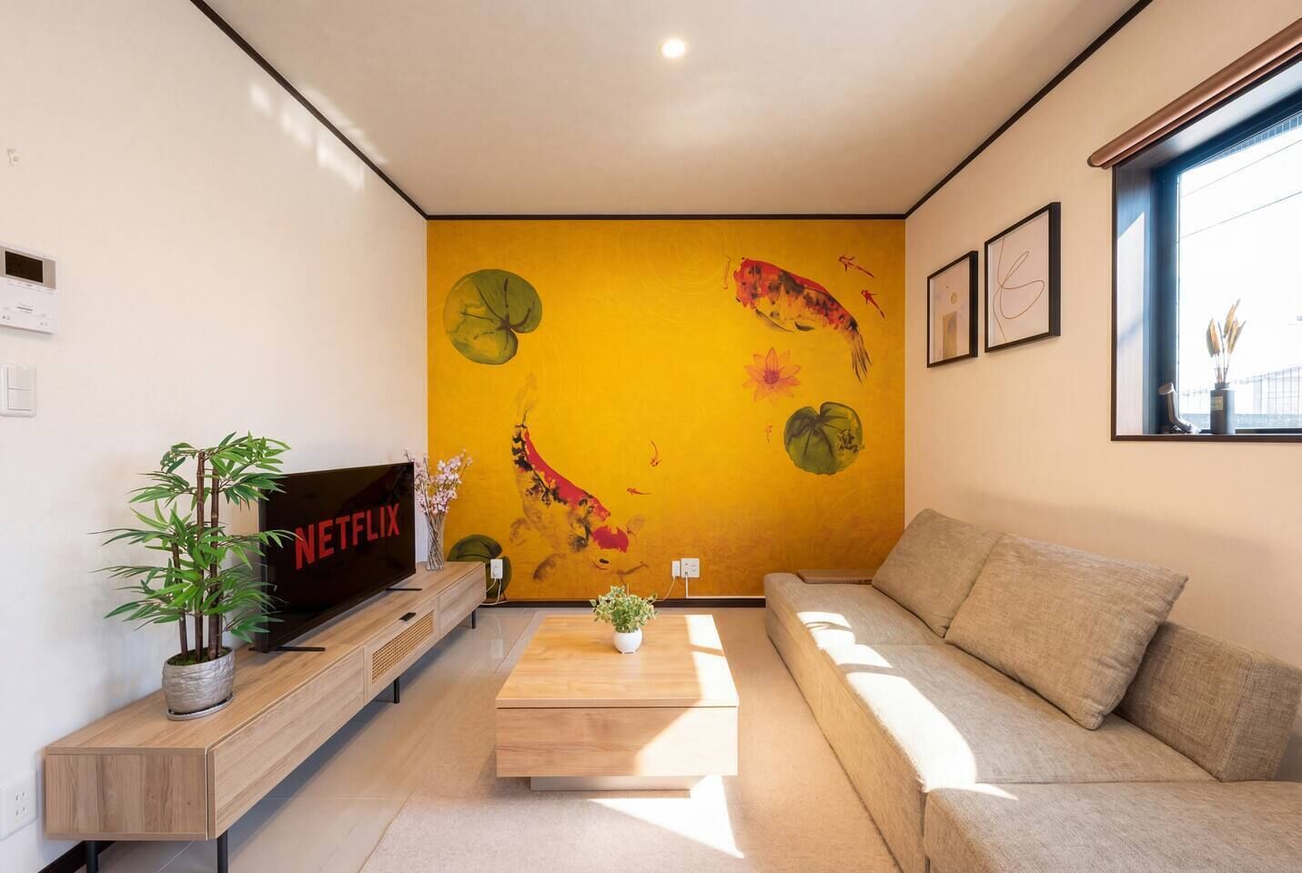 A living room with a sofa, a coffee table, a TV, and a wall with a yellow mural.