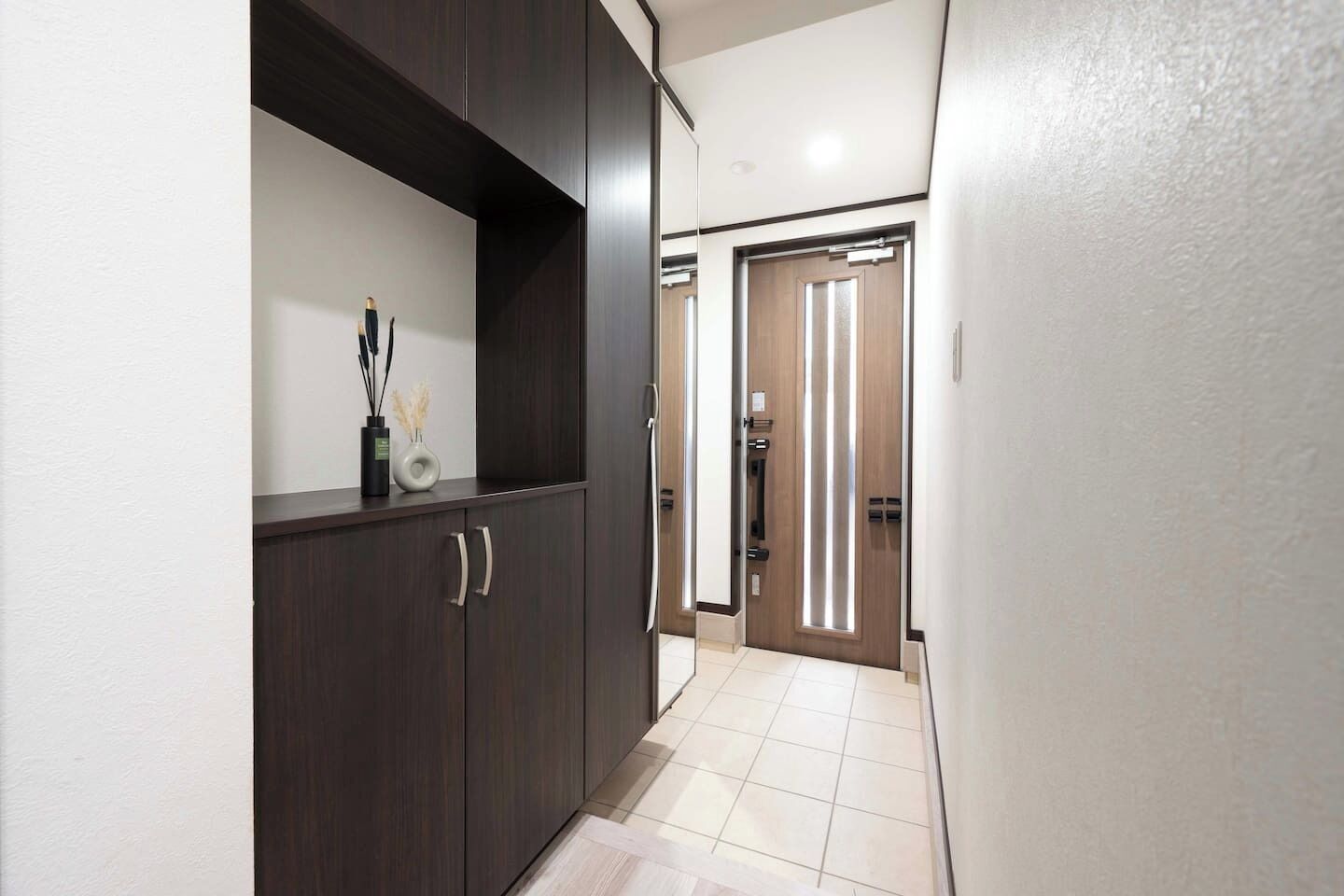 A hallway with a dark wooden cabinet, a door with vertical light strips, and a tiled floor.