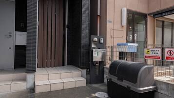 A building entrance with a mailbox, a security camera, and a metal fence with a sign.