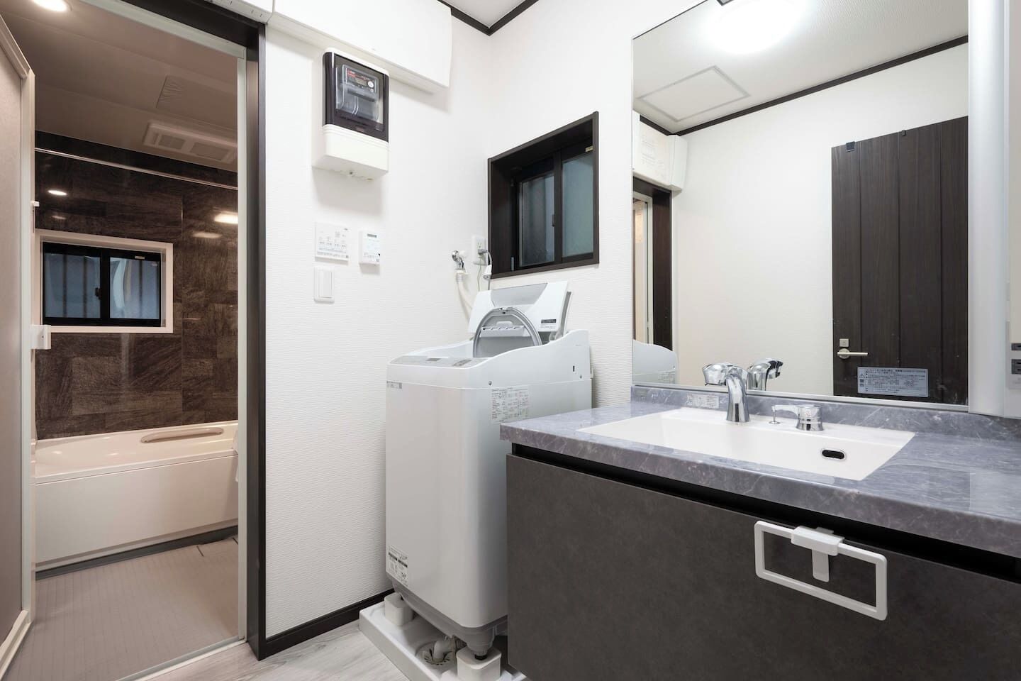 Een moderne badkamer met een ingebouwde wasmachine en droger, een grote spiegel en een wastafel met een marmeren aanrechtblad.