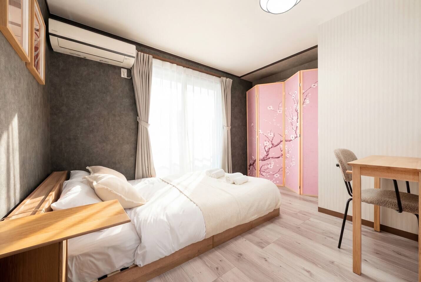 A modern bedroom with a bed, a desk, and a view of cherry blossoms.