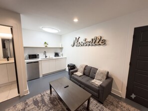 A modern living room with a grey sofa, a coffee table, and a wall-mounted sign that reads 'Nashville'. - Cozy 1BR w/ King Bed • Minutes to Downtown (Nashville)