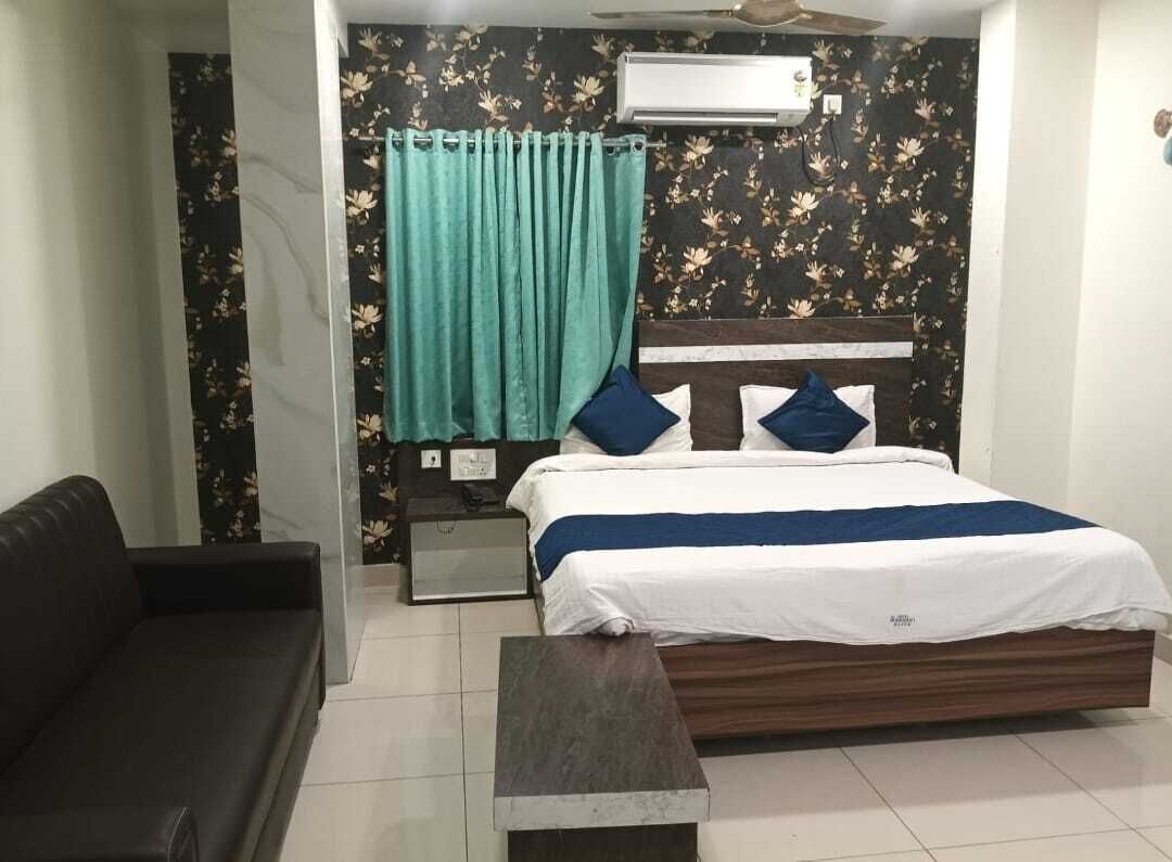 A bedroom with a bed, a nightstand, a sofa, and a window with curtains.