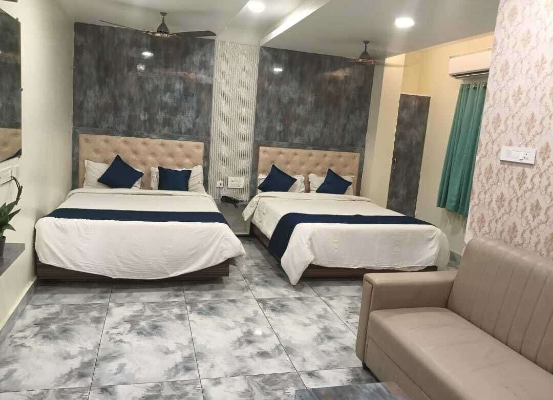 A hotel room with two beds, a sofa, a ceiling fan, and a bathroom with a shower curtain.