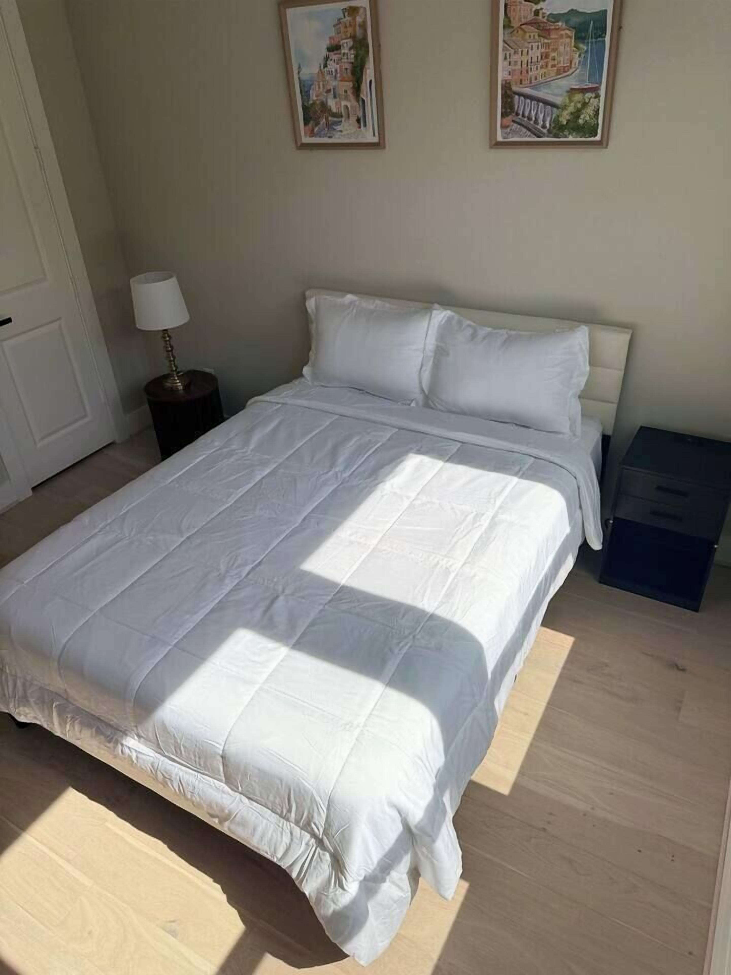 A bedroom with a large bed, a bedside table, a lamp, and two framed pictures on the wall.