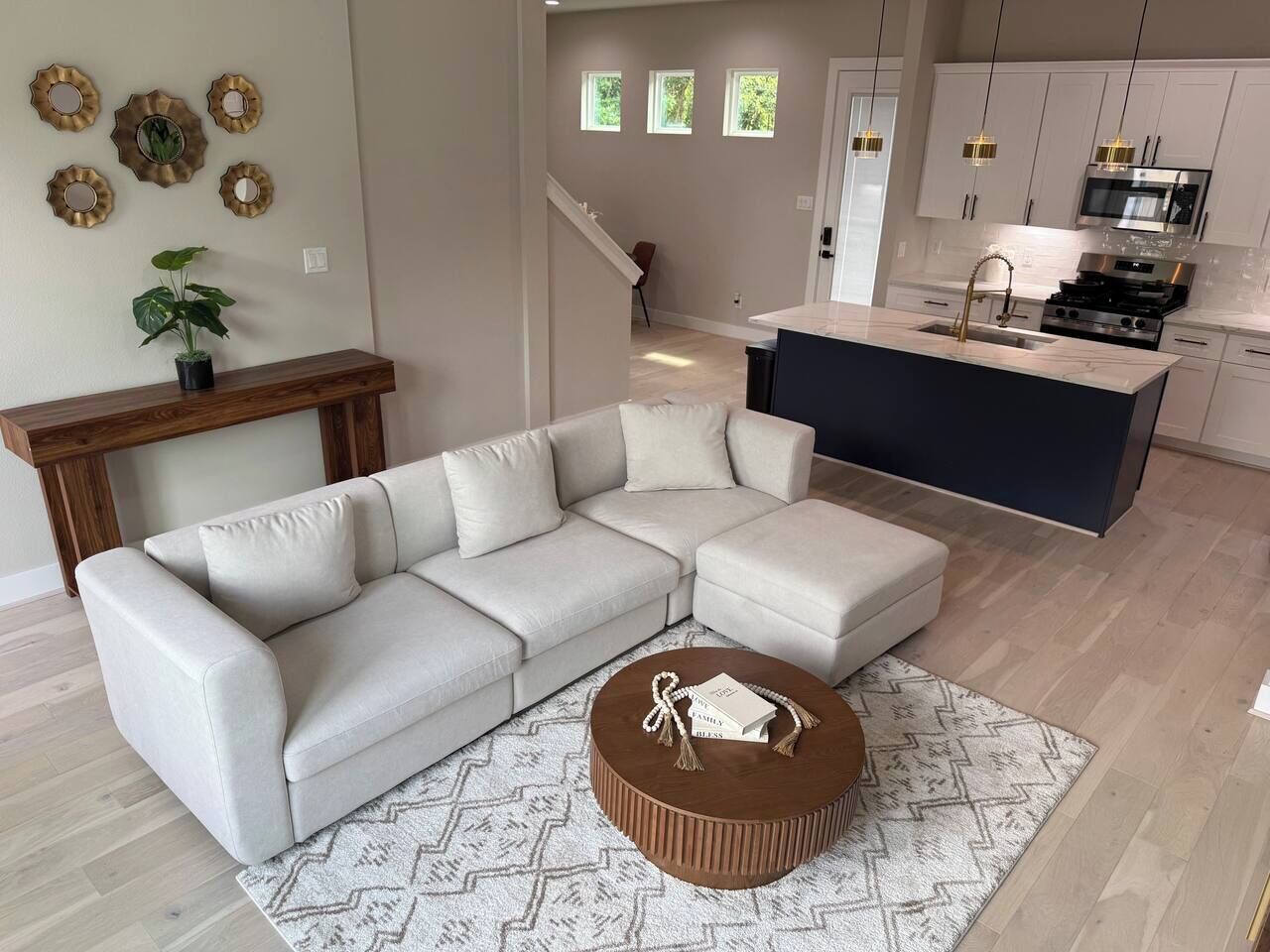A modern living room with a sectional sofa, a round coffee table, and a kitchen area with a central island.