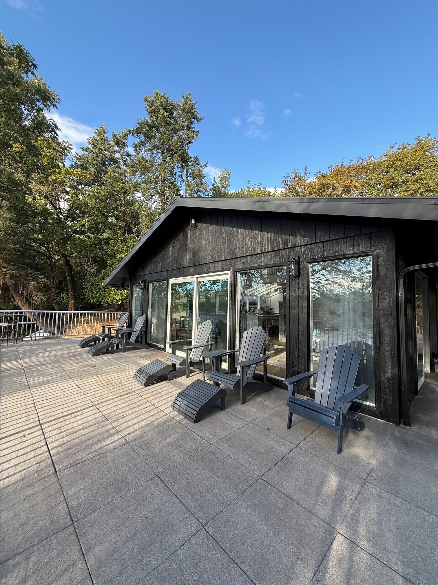 A modern outdoor seating area with Adirondack chairs and a patio table, surrounded by glass doors leading to a building.