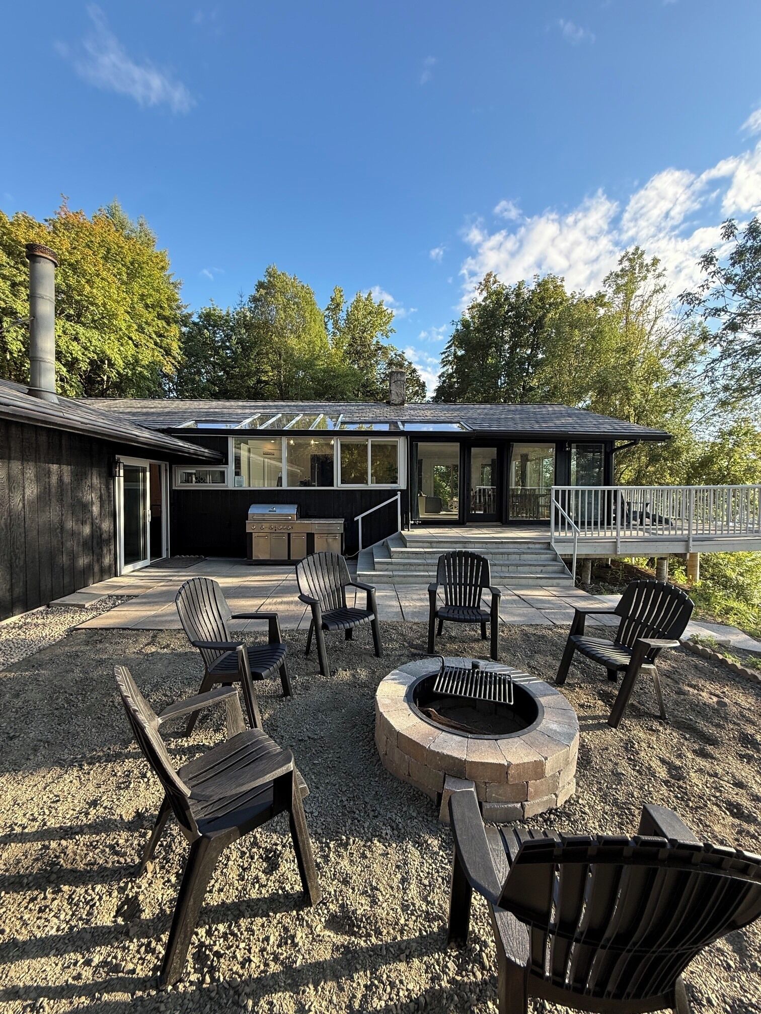 A modern outdoor patio with Adirondack chairs, a fire pit, and a grill area.