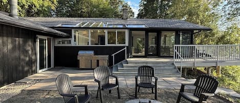 A modern outdoor patio with Adirondack chairs, a fire pit, and a grill area.