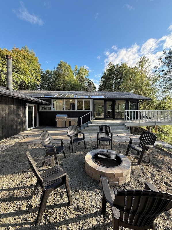 A modern outdoor patio with Adirondack chairs, a fire pit, and a grill area.