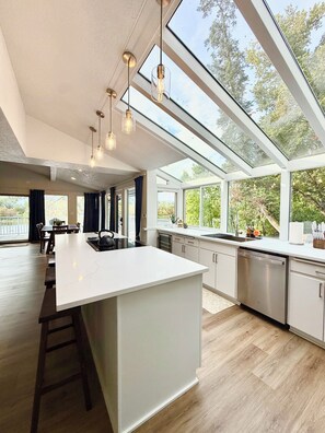 A modern kitchen with a large island, pendant lights, and a view through large windows. - Willamette Riverfront Estate - Wine County. Secluded on 2.5 acres w/Deck Views. (Salem)