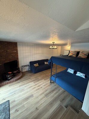 A compact living space with a sofa, a TV, a small table, and a brick wall.