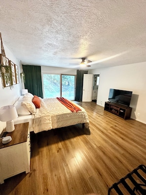 A bedroom with a bed, bedside table, lamp, and a TV stand with a flat-screen TV.