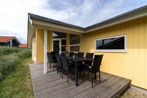 En gul byggnad med en terrass, ett bord med stolar och ett fönster.