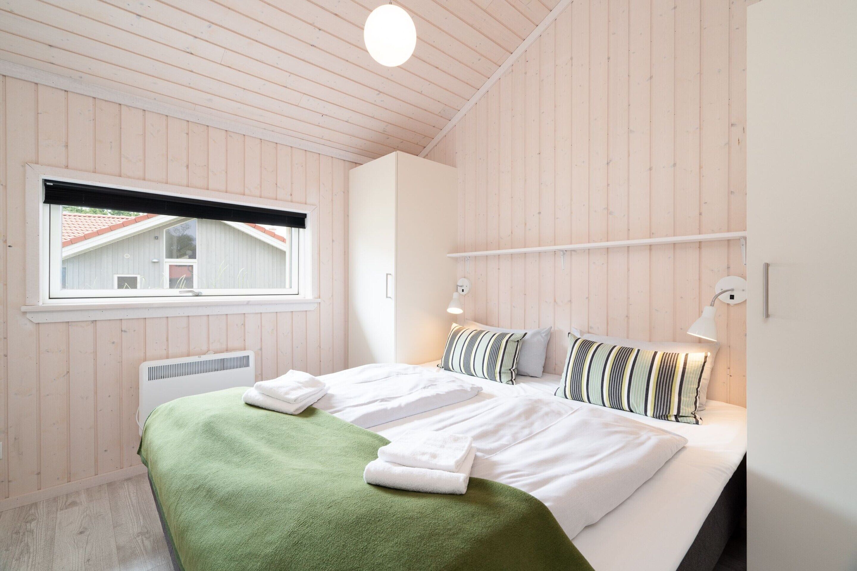 A bedroom with a bed, a window, a radiator, and a wall-mounted light fixture.