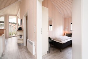 A modern bedroom with a bed, bedside table, and a desk with a chair. There is a radiator under the desk and a window with a view of the outside.