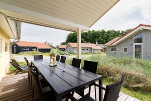 A covered outdoor dining area with a wooden table and chairs, surrounded by a deck.