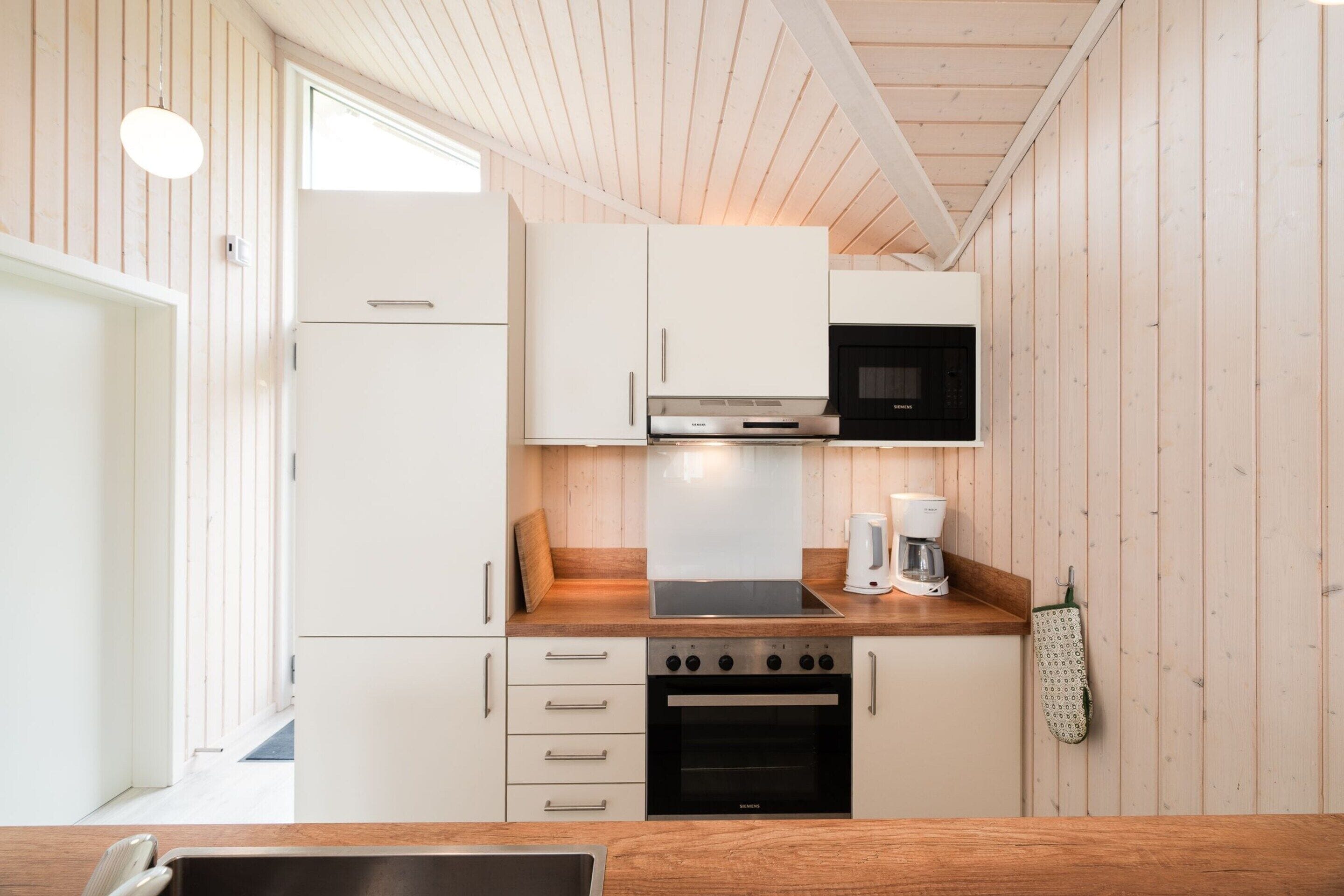 A compact kitchen with white cabinets, a black microwave, a Siemens oven, and a coffee maker.