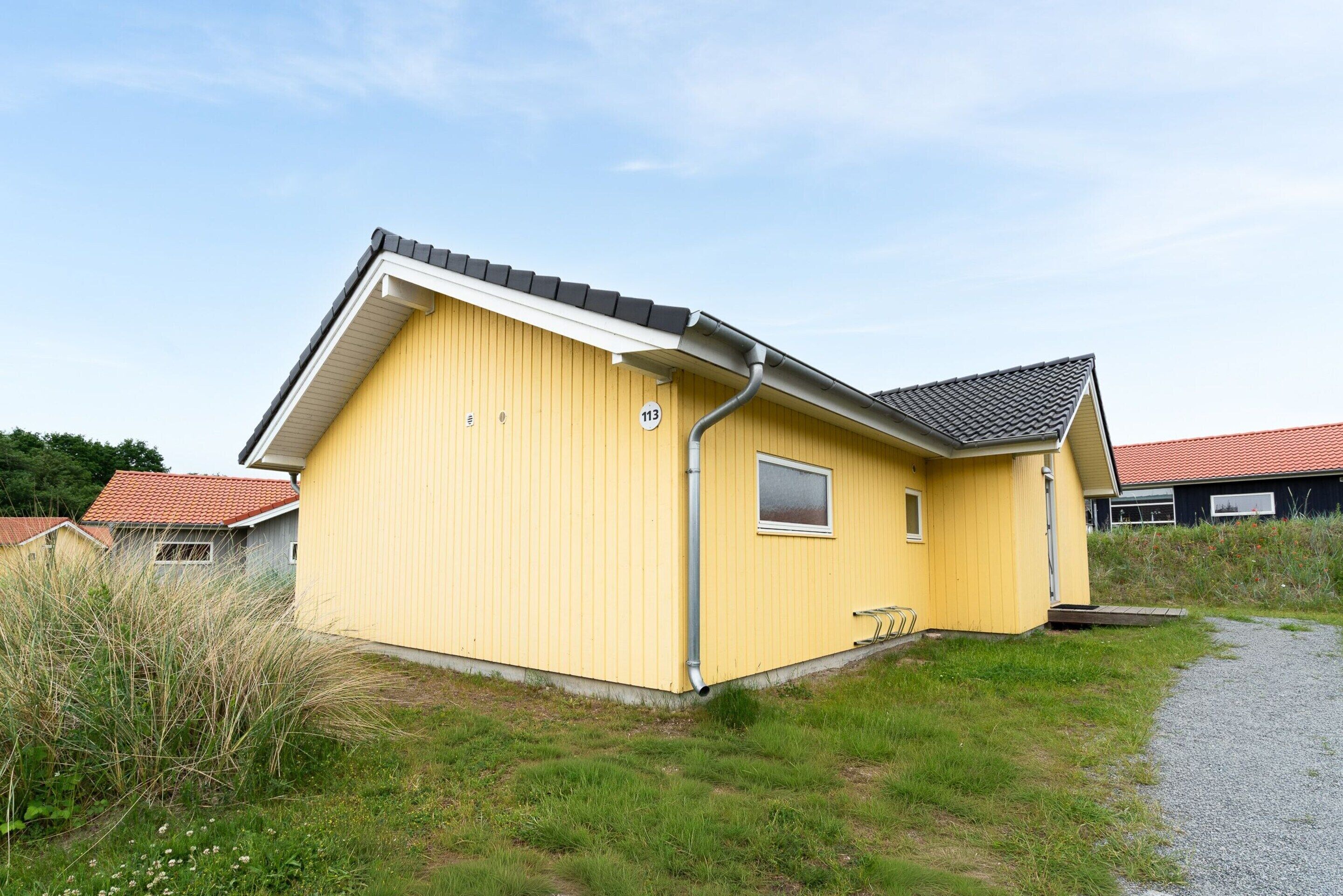 A yellow single-story house with a grey roof, a small window, and a number '113' on the side.