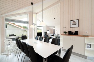 Eine moderne Küche mit Essbereich, ausgestattet mit einem großen Tisch, Stühlen, Pendelleuchten und Blick ins Freie.