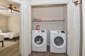 A laundry room with two front-loading washing machines, a ceiling fan, and a shelf with laundry supplies. - Waterfront 3-bedroom House in Lake Community with Mountain View (Glendale)