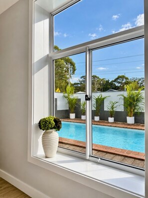 Ein Fenster mit Blick auf einen Swimmingpool, Topfpflanzen und einen klaren Himmel.