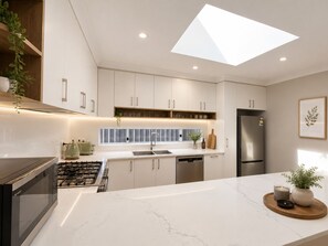 Eine moderne Küche mit weißen Schränken, einem Edelstahlkühlschrank, einem Gasherd und einem Oberlicht.