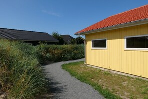Ein gelbes Gebäude mit rotem Dach, einem Kiesweg und umgebender Bepflanzung.