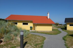 Ein gelbes Gebäude mit rotem Dach, Schornstein und einer kleinen, grünen Mülltonne.