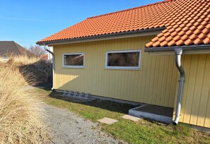 A yellow building with a red-tiled roof, two windows, and a gravel driveway. - Skandinavisches Chalet fur 10 Personen (Grossenbrode)