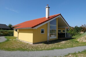 A yellow single-story house with a red-tiled roof, a chimney, and a covered porch with outdoor seating. - Skandinavisches Chalet fur 10 Personen (Grossenbrode)