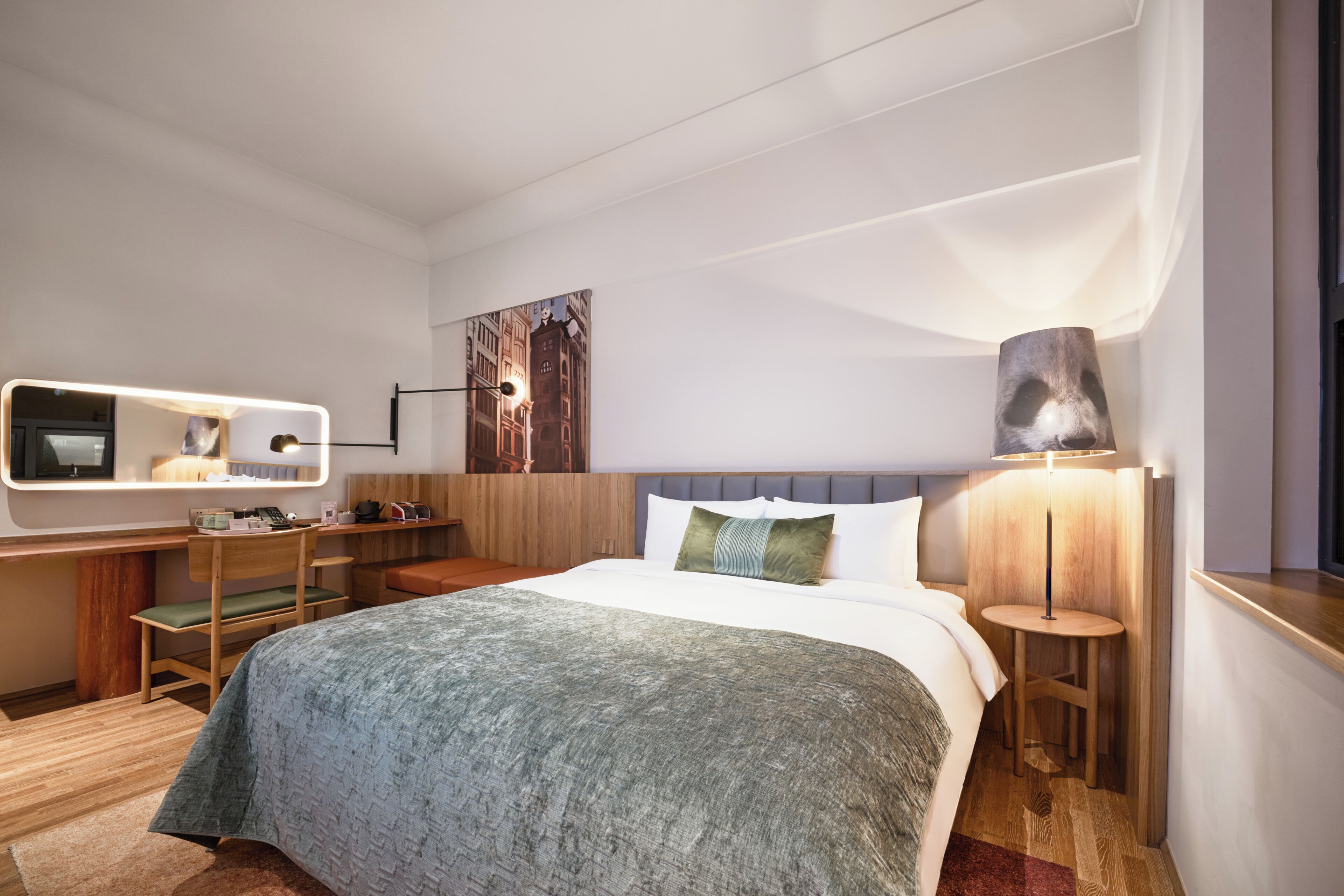 Quarto de hotel com cama, mesas de cabeceira, escrivaninha, cadeira, abajur e um quadro na parede.