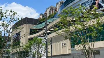 Un edificio moderno con un gran anuncio, mesas al aire libre y un área ajardinada con árboles.