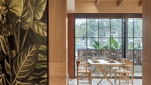Un comedor con un gran ventanal, mobiliario de madera y un panel decorativo con diseño de hojas.