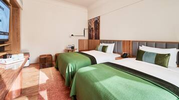 A hotel room with two beds, a TV, a small table with a kettle and bottles, and a painting on the wall.