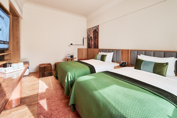 Habitación de hotel con dos camas, televisión, una mesita con hervidor y botellas, y un cuadro en la pared.